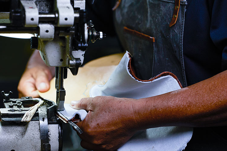 Hands sewing leather boots together.